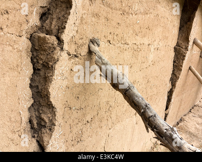 A cracked and leaning section of mud-brick wall being supported by a wooden prop Stock Photo