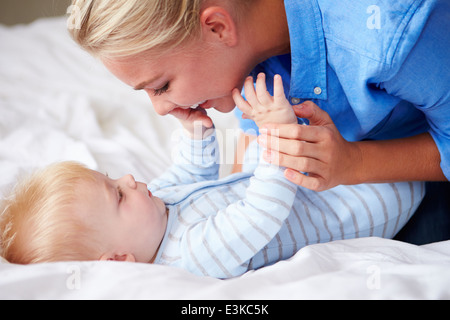 Mother Playing With Baby Son As They Lie In Bed Together Stock Photo