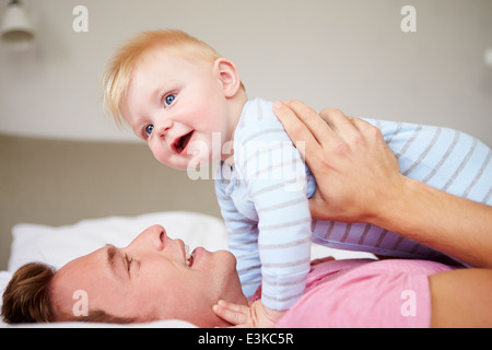 Father Playing With Baby Son As They Lie In Bed Together Stock Photo