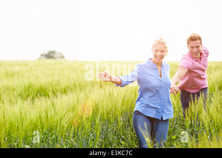 Romantic Couple Running In Field Holding Hands Stock Photo