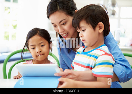 Mother Helping Children With Homework Using Digital Tablet Stock Photo