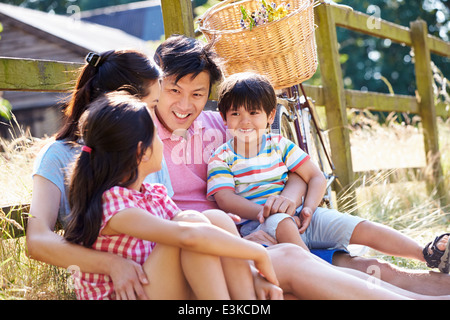 Asian Family Resting By Fence With Old Fashioned Cycle Stock Photo