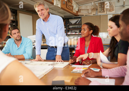 Male Boss Leading Meeting Of Architects Sitting At Table Stock Photo