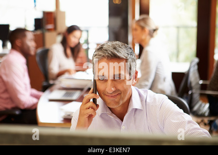 Businessman On Phone At Desk With Meeting In Background Stock Photo