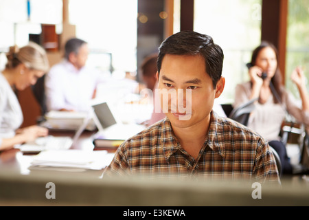 Businessman Working At Desk With Meeting In Background Stock Photo