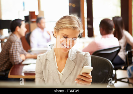Businesswoman Working At Desk Using Mobile Phone Stock Photo