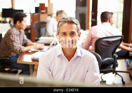 Businessman Working At Desk With Meeting In Background Stock Photo