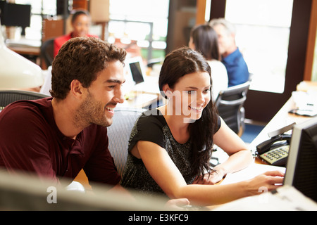 Two Colleagues Working At Desk With Meeting In Background Stock Photo
