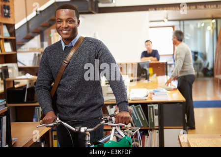 Architect Arrives At Work On Bike Pushing It Through Office Stock Photo