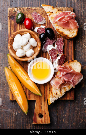 Prosciutto ham, Slices of melon cantaloupe, Mozzarella cheese and Olives on cutting board Stock Photo