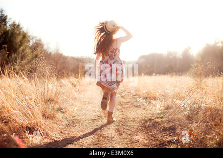 Rear view of young woman (18-19) walking along dirt road Stock Photo
