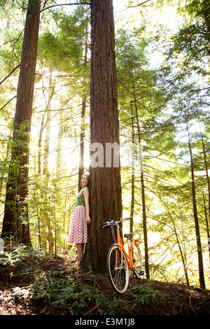 Woman leaning against tree in forest Stock Photo