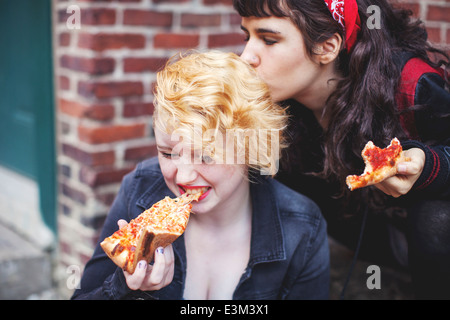 Young woman kissing her friend while eating pizza Stock Photo