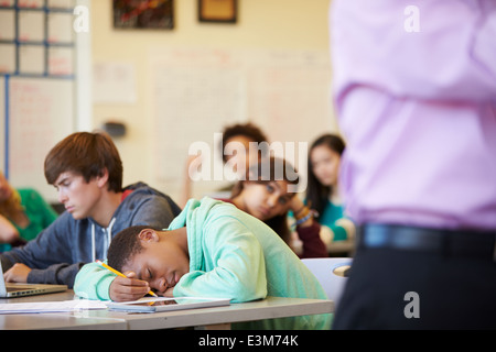 Bored High School Pupil Slumped On Desk In Classroom Stock Photo