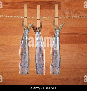 Three typical Dutch salted herring called maatje or zoute haring hanging on a rope with clothespin Stock Photo