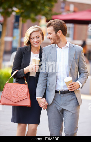 Business Couple Walking Through Park With Takeaway Coffee Stock Photo