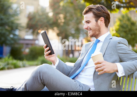 Businessman On Park Bench With Coffee Using Digital Tablet Stock Photo