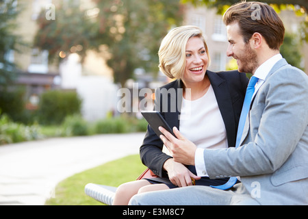 Business Couple Using Digital Tablet On Park Bench Stock Photo