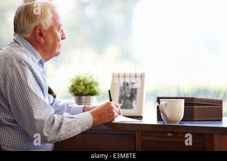 Senior Man Writing Memoirs In Book Sitting At Desk Stock Photo