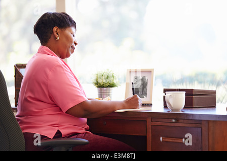 Mature Woman Writing In Notebook Sitting At Desk Stock Photo