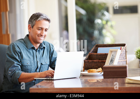 Mature Hispanic Man Using Laptop On Desk At Home Stock Photo