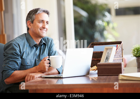 Mature Hispanic Man Using Laptop On Desk At Home Stock Photo