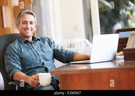 Mature Hispanic Man Using Laptop On Desk At Home Stock Photo