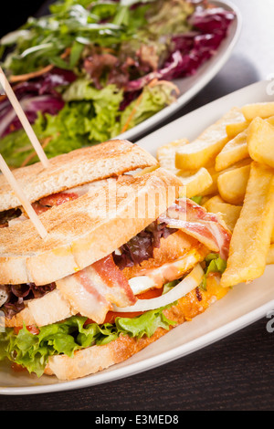 Club sandwich on toasted white bread with a meat filling served with crispy golden potato French fries, closeup partial view isolated on white Stock Photo