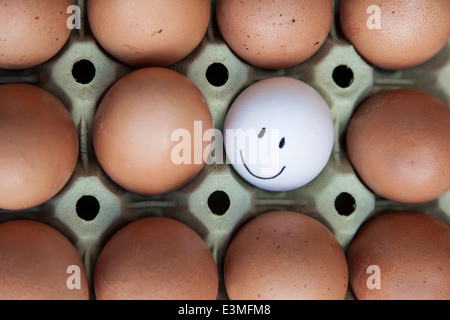 Single white egg with happy faces surrounded by blank brown eggs. Stock Photo