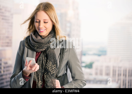 Smiling businesswoman using cell phone in urban window Stock Photo