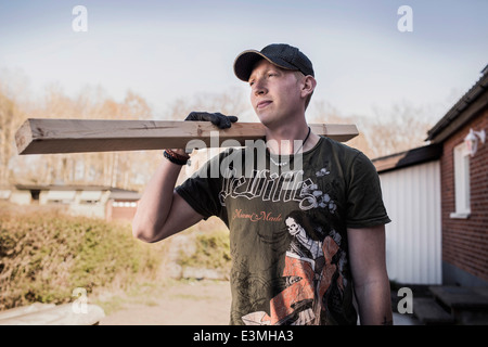 Male carpenter carrying wooden plank at construction site Stock Photo