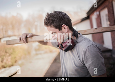 Carpenter carrying wooden plank at construction site Stock Photo