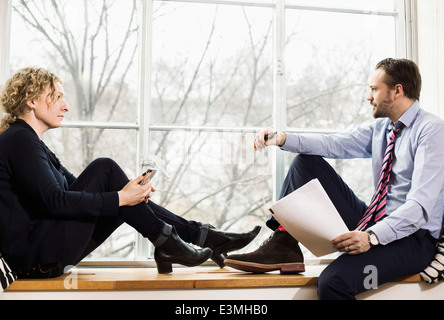 Full length of business people sitting on ledge by window Stock Photo