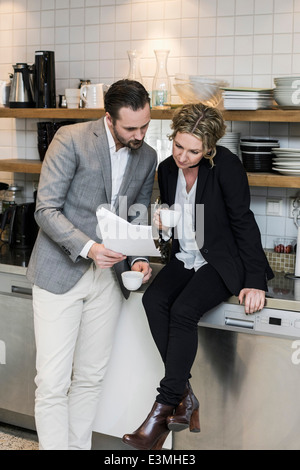 Business people having coffee while reading document at kitchen counter Stock Photo