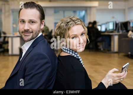 Portrait of confident businessman and businesswoman sitting back to back in office Stock Photo