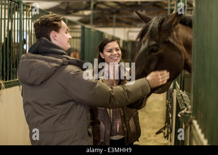 Happy young couple stroking horse in stable Stock Photo