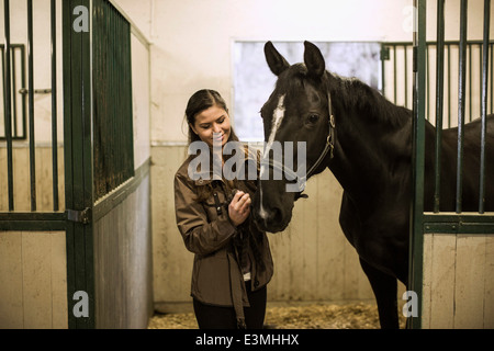 Smiling young woman with horse in stable Stock Photo