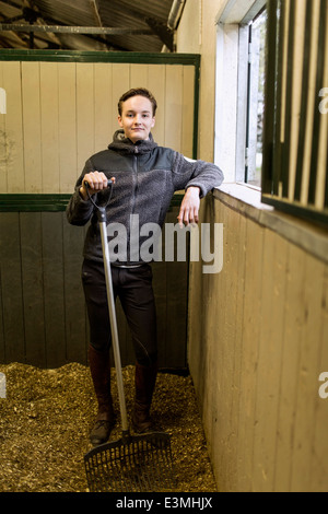 Full length portrait of confident young man with pitchfork in horse stable Stock Photo