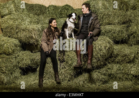 Full length rear view of happy young couple with dog sitting on hay stack in stable Stock Photo