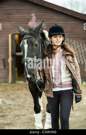 Young woman with horse walking outside barn Stock Photo