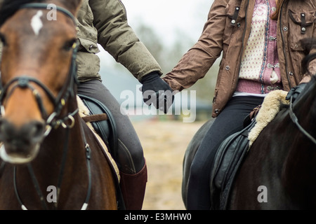 Low section of couple holding hands while riding horses Stock Photo