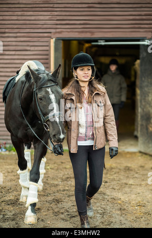 Young woman with horse walking outside barn with man in background Stock Photo