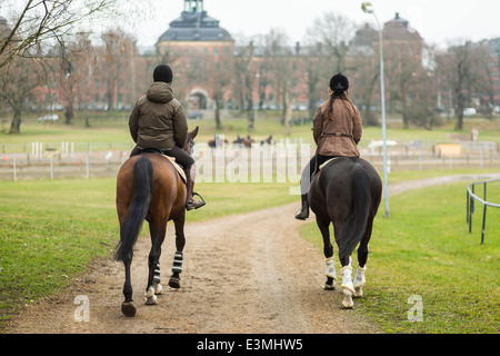 Full length rear view of young couple riding horses on dirt road Stock Photo