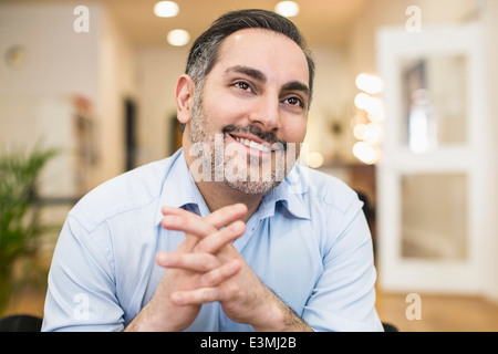 Smiling businessman with hands clasped looking away in office Stock Photo