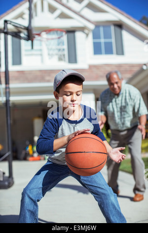 Grandfather and grandson playing basketball in driveway Stock Photo