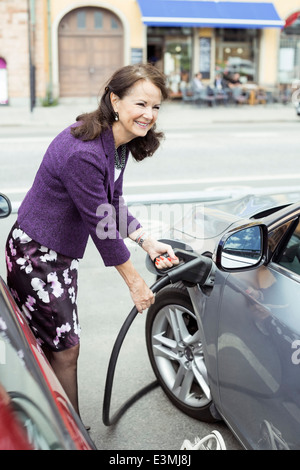 Smiling senior woman refueling car on street Stock Photo