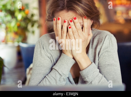 Sad young woman sitting with head in hands at home Stock Photo