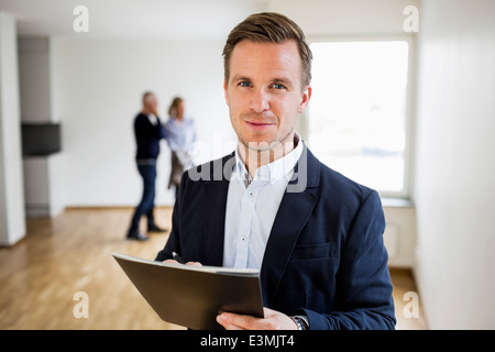 Portrait of confident real estate agent with couple standing in background at home Stock Photo