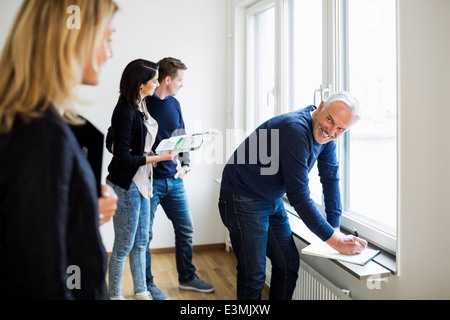 Smiling mature real estate agent looking at colleague white couple looking through window at home Stock Photo