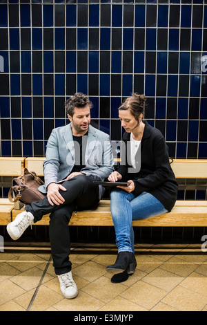 Full length of business people discussing over digital tablet while sitting on bench at subway station Stock Photo